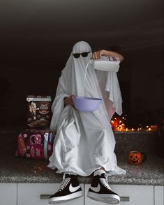 a person in a ghost costume holding a bowl and wearing black converse shoes, standing on top of a counter