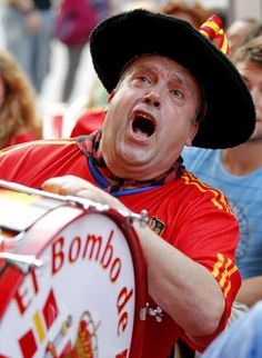 a man in a black hat and red shirt with his mouth open while holding a drum