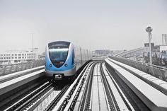 a blue and silver train traveling down tracks next to tall buildings on either side of it