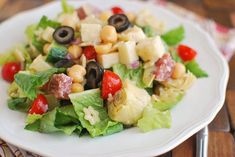 a salad with olives, lettuce and tomatoes is on a white plate