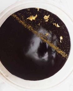 a black cake with gold sprinkles in a white bowl on a table