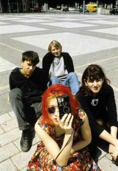 four people sitting on the ground with one holding a camera in front of their face