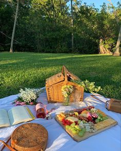 an open book on a table with food and wine in front of it, near a picnic basket