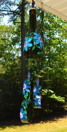 a wind chime with blue flowers hanging from it's side in front of trees