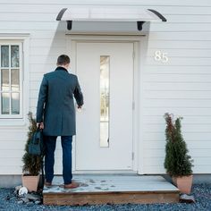 a man in a suit and tie holding a suitcase standing outside the front door of a white house