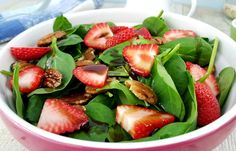 a pink bowl filled with spinach and strawberries on top of a white table