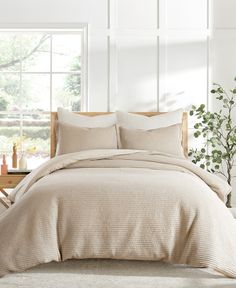 a bed with beige linens and pillows in a white room next to a window