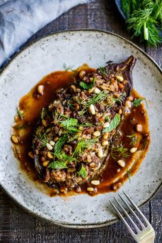 a white plate topped with meat covered in gravy and garnished with herbs