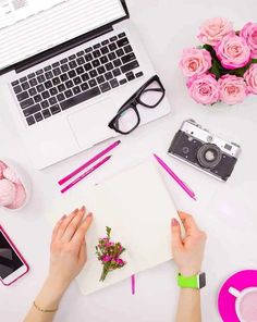 a woman's hands on top of a notebook surrounded by pink flowers and other office supplies