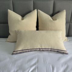 two pillows sitting on top of a bed with white sheets and grey headboard behind them