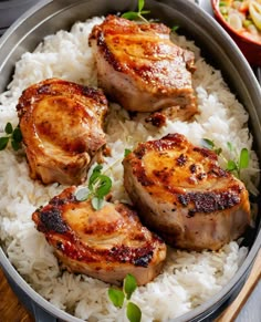 three pieces of meat on top of rice in a pan with chopsticks next to it