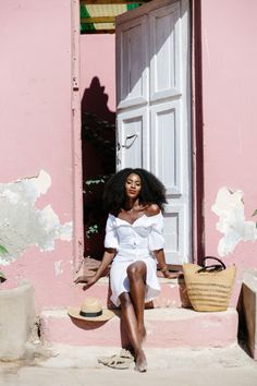 a woman sitting on steps in front of a pink building with white door and window