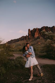 a man and woman hugging each other in front of the desert mountain range at sunset