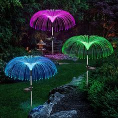 three colorful lights in the shape of palm trees are lit up at night, with grass and rocks surrounding them