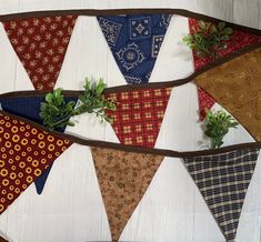 an assortment of different colored bandanas hanging on a white wooden wall next to plants