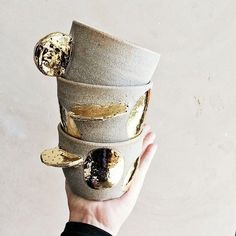 a person holding up a cup with gold leaf decorations on the top and bottom, in front of a white wall