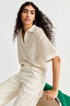 a woman sitting on top of a chair wearing white pants and a knitted shirt