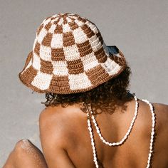 a woman sitting on the ground wearing a brown and white hat with pearls around her neck