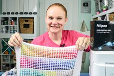 a woman holding up a piece of fabric in front of a printer and other crafting supplies