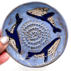 a hand holding a small blue plate with two dolphins on it's side and another one in the background