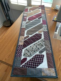 a long table runner made out of quilts on top of a wooden floor next to a window