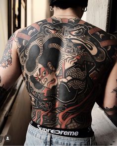 the back of a man with tattoos on his upper and lower half, standing in front of a window