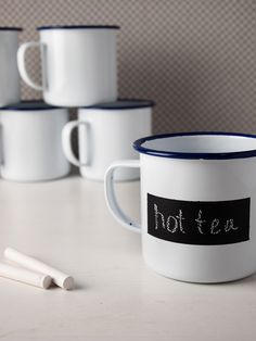 four coffee mugs with writing on them sitting next to one another and two pens