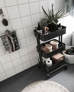 a bathroom with white tiles and black shelves filled with toilet paper, plants and other items