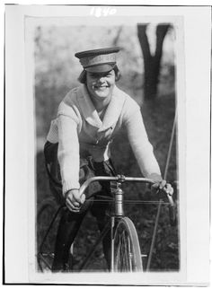 an old black and white photo of a woman on a bicycle wearing a sailor's hat