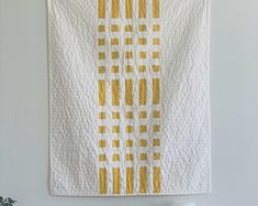 a white and yellow quilt hanging on the wall next to a vase filled with flowers