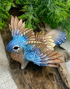 a blue and brown bird statue sitting on top of a wooden log next to a plant