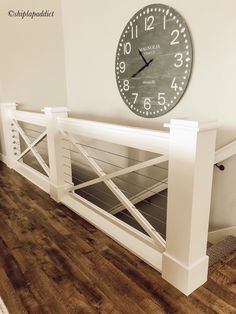 a clock mounted to the side of a wall next to a wooden floor and white railing