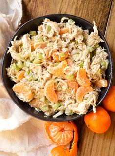 a black bowl filled with chicken salad next to oranges