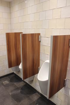 three urinals in a public restroom with wood panels on the wall and tile floor