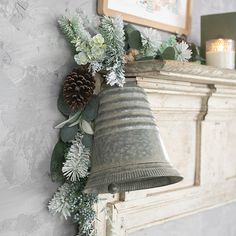 a bell hanging from the side of a wall with greenery and pine cones on it