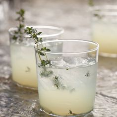 two glasses filled with ice and herbs on top of a table next to each other