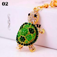 a green turtle keychain sitting on top of a white box with a gold chain