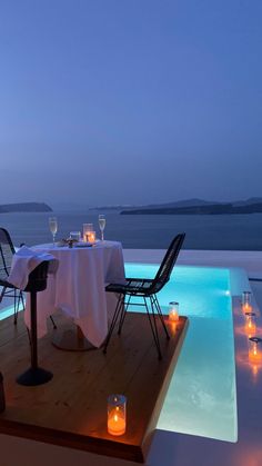 an outdoor dining area with candles on the table and water in the pool behind it