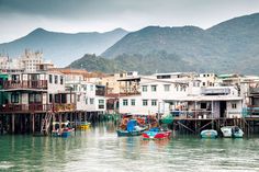 several boats floating in the water next to houses on stilts with mountains in the background