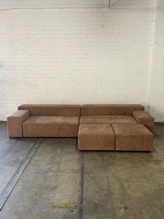 a brown couch sitting on top of a floor next to a white brick wall in an empty room