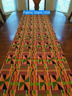 an orange, green and black table cloth on a wooden floor with windows in the background