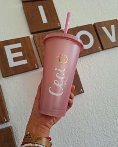 a person holding up a pink drink in front of some wooden blocks with the word love spelled on it