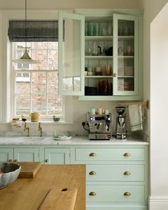 a kitchen filled with lots of green cupboards next to a counter top and window