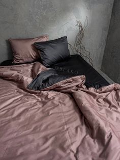 an unmade bed with pink sheets and black pillow cases in a room that has concrete walls