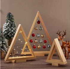 three wooden christmas trees with ornaments on them and one has a deer figurine next to it