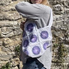 a woman is holding a crocheted bag in front of a stone wall