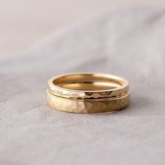 two gold wedding rings sitting on top of a white cloth covered bed sheet, with one ring in the middle