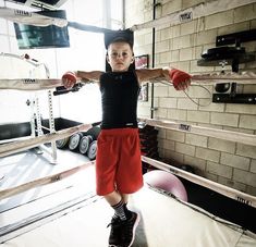 a young boy standing in the middle of a boxing ring wearing red shorts and black shirt