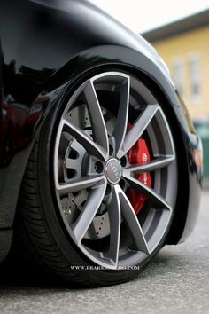 the front wheel of a black car with red brake pads on it's rim