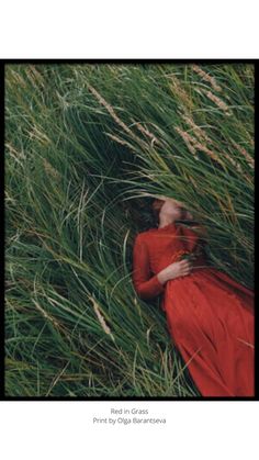 a woman in a red dress laying on the ground surrounded by tall grass, with her eyes closed